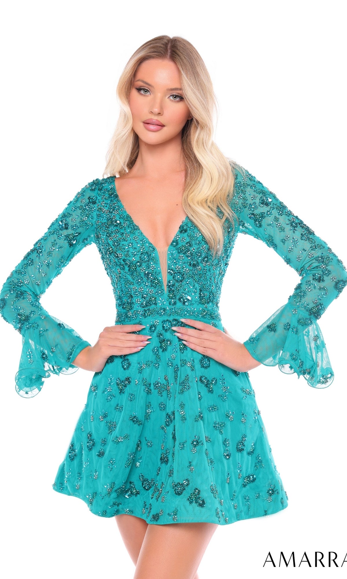 A woman poses with hands on hips in the Short Homecoming Dress 88032 by Amarra—a teal, beaded mini dress featuring long sleeves, sequin and bead embellishments, a deep V-neck, and flared cuffs—against a white background.